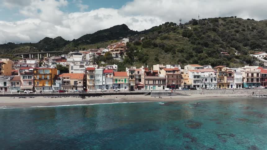 An aerial shot slowly approaches a charming coastal town in Sicily, Italy, revealing colorful houses along the beach