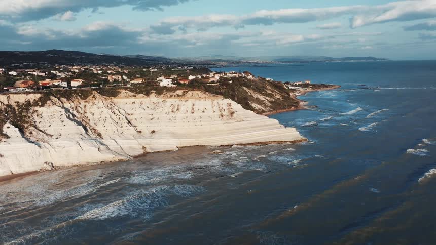 Aerial view of the dramatic white cliffs of Scala dei Turchi on the coast of Sicily, with waves rolling in from the sea