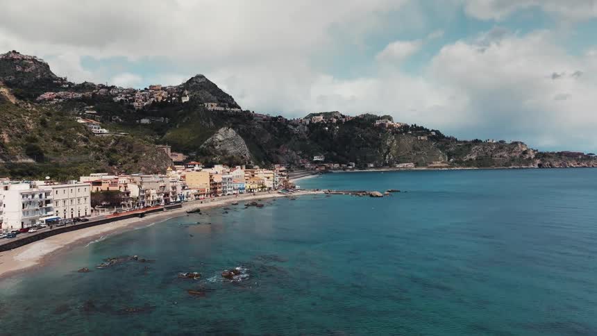 A static aerial view of a picturesque coastal town nestled between rolling green hills and the clear blue ocean