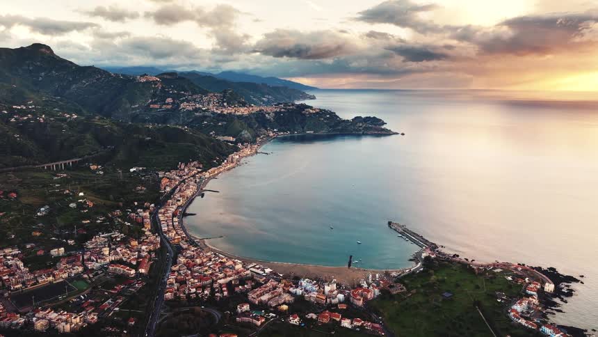 A serene and picturesque aerial cinemagraph captures a coastal town in a beautiful bay surrounded by green mountains at sunset
