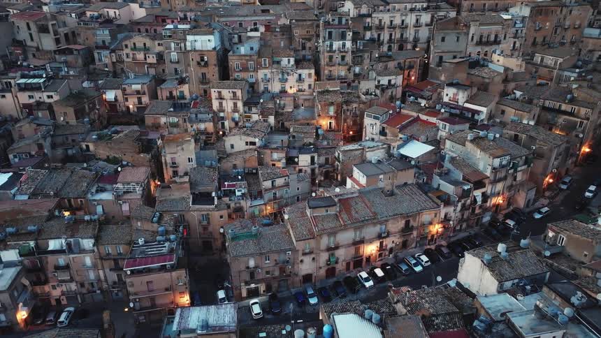 The rooftops of a historic European city glow with warm light during a tranquil twilight evening