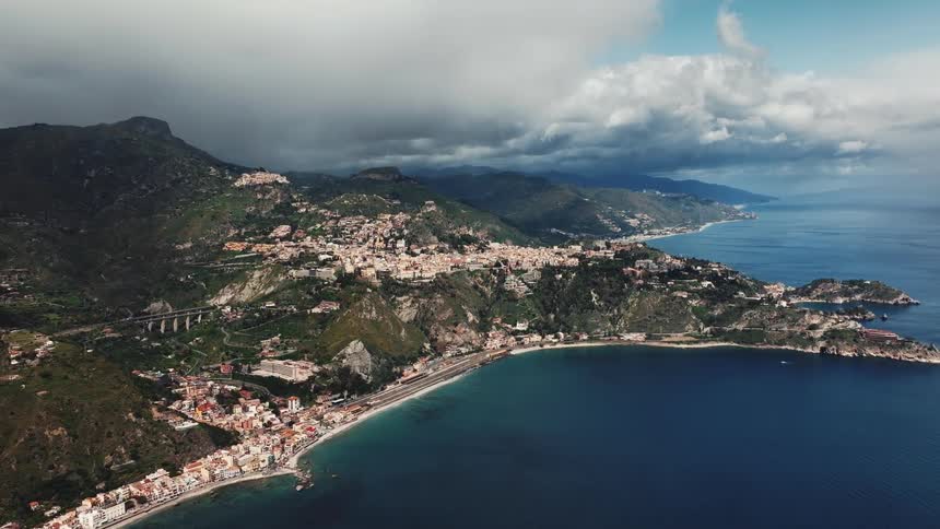 A stunning aerial view of a picturesque town on the Italian coast, nestled between mountains and the sea under a dramatic cloudy sky
