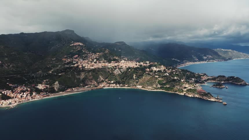 A stunning aerial view of a picturesque coastal town nestled in the mountains along the sea under a dramatic, cloudy sky