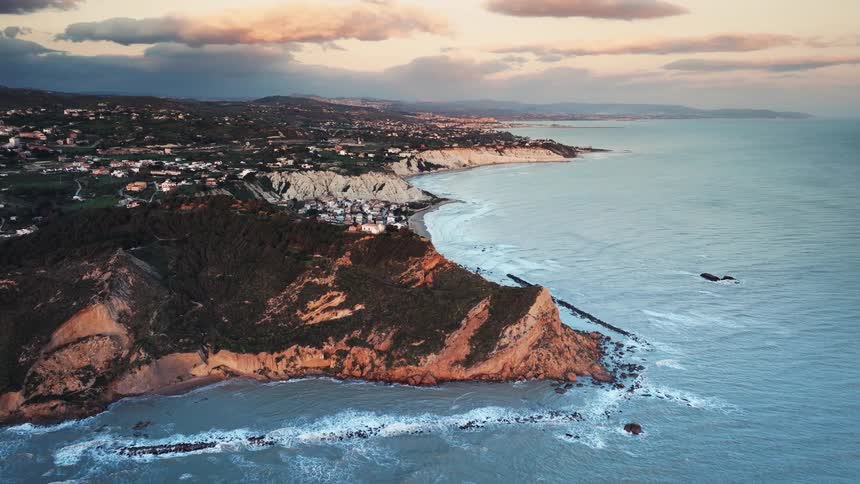 Stunning aerial view of a rugged coastline with a lush, green headland and a seaside town glowing under a beautiful sunset sky