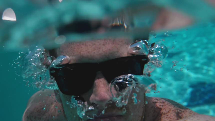 A man dives underwater with sunglasses on