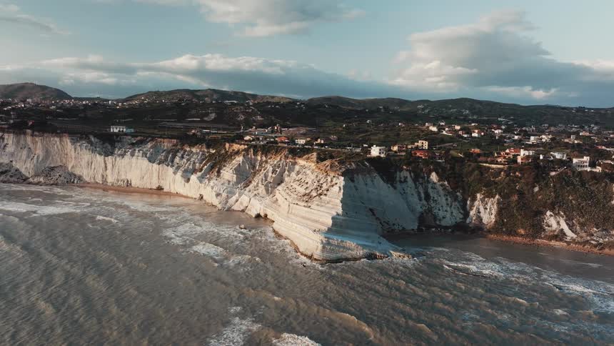 Aerial view of the iconic white cliffs of Scala dei Turchi in Sicily as waves from the sea crash against the coast during a beautiful sunset