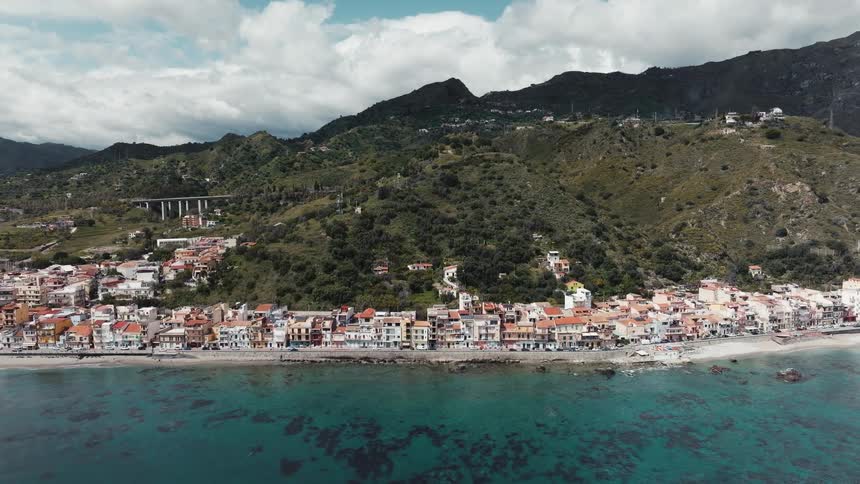 Static aerial view of a picturesque coastal village nestled against a lush green mountain in Sicily