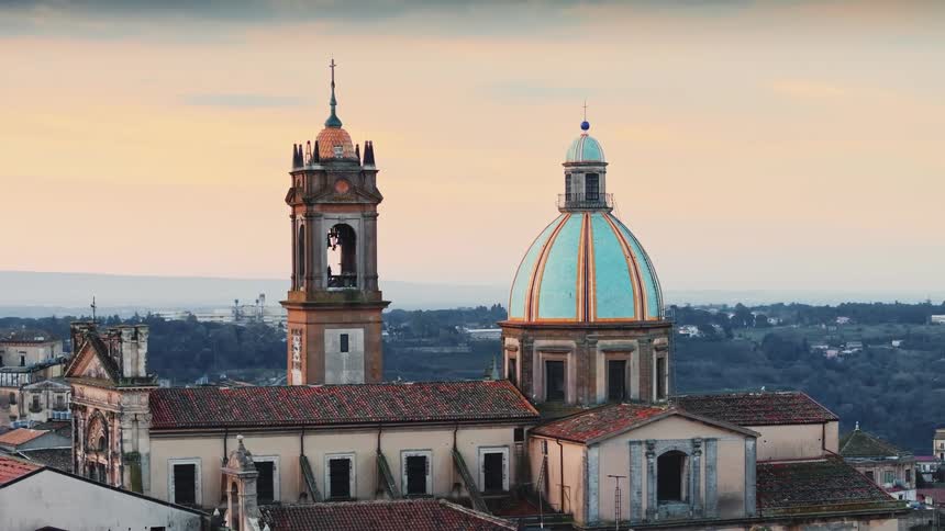 The bell in the historic tower of an old Italian cathedral with a striking blue dome begins to toll at sunset