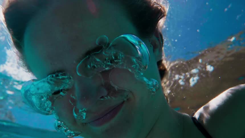 Woman under water is smiling and blowing air bubbles from her nose