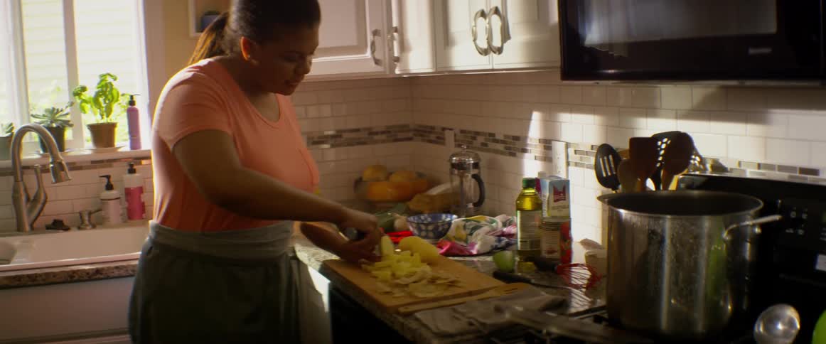 A woman chops potatoes on a cutting board in the kitchen