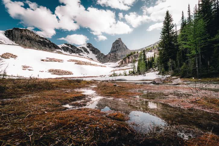 A stunning timelapse captures clouds drifting over a snowy mountain valley, its peaks beautifully reflected in the clear spring meltwater below