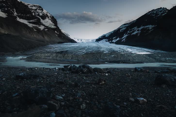 A dramatic timelapse captures the transition from dusk to a starlit night over a vast glacier nestled in a mountain valley