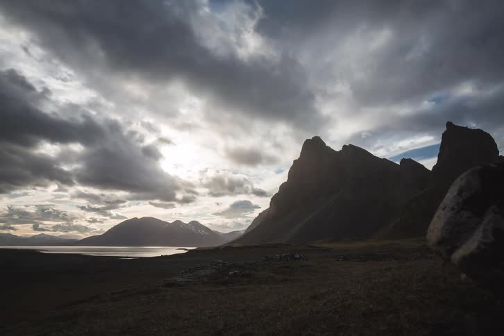 A dramatic time-lapse of clouds moving swiftly over a silhouetted mountain range as the sun shines brightly over a coastal landscape