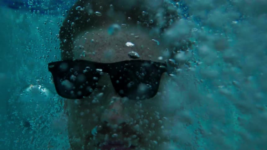 A man wearing sunglasses is underwater amidst a lot of bubbles