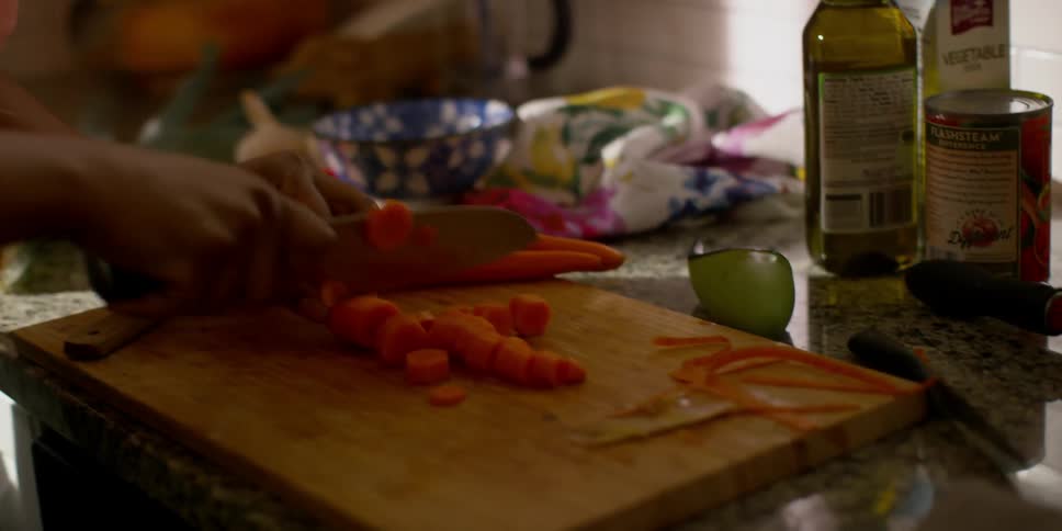 Woman dancing in kitchen while chopping up carrots with knife