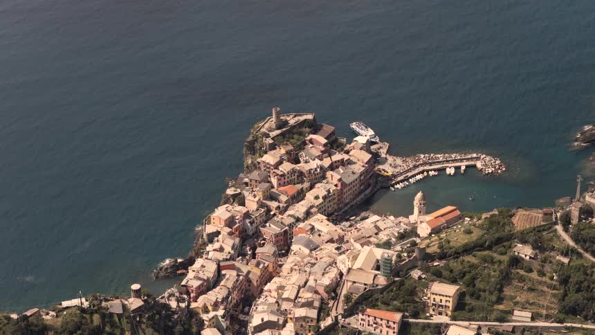 A slow aerial zoom-in reveals the picturesque coastal village of Vernazza in Cinque Terre, Italy, nestled on a cliffside overlooking the Ligurian Sea