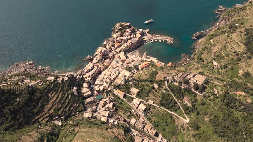 High-angle aerial view of the historic Italian village of Vernazza in Cinque Terre, nestled between terraced hillsides and the azure Ligurian Sea