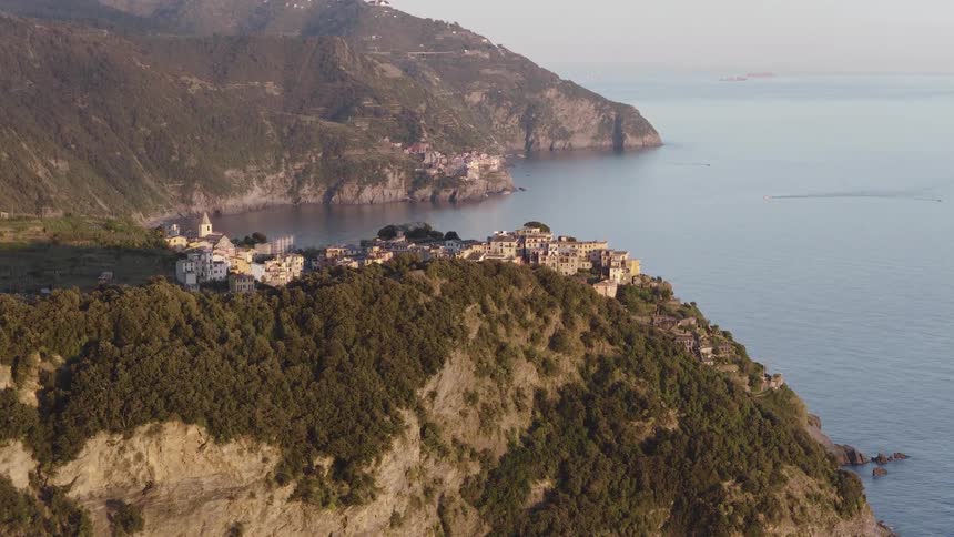 Slowly rising aerial footage captures the breathtaking beauty of Corniglia, one of the Cinque Terre villages, clinging to a dramatic cliffside over the sea at sunset