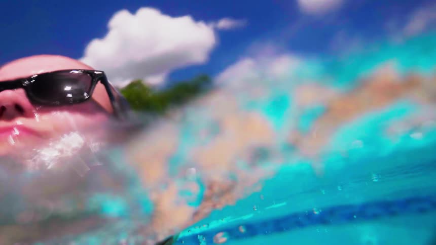 A woman wearing sunglasses surfaces in a swimming pool