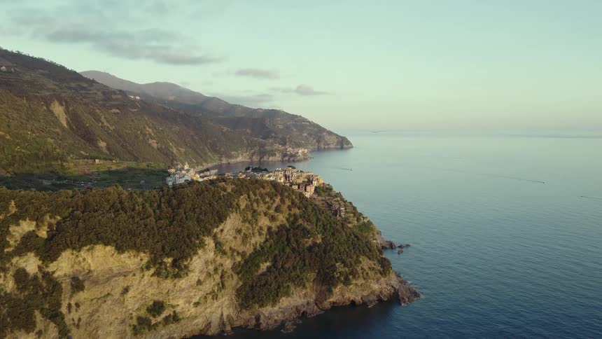 A stunning aerial view reveals the charming coastal village of Corniglia in Italy's Cinque Terre, nestled on a cliff above the serene sea at sunrise
