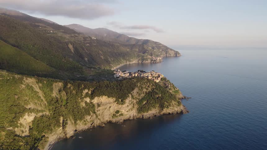 A serene aerial view of the historic village of Corniglia in Cinque Terre, Italy, perched atop a dramatic cliff overlooking the calm sea at sunrise