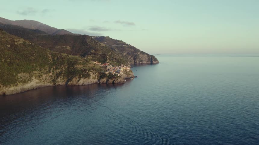 A stunning static aerial view of the Cinque Terre coastline in Italy with a beautiful village perched on the cliffs overlooking the calm ocean at sunrise