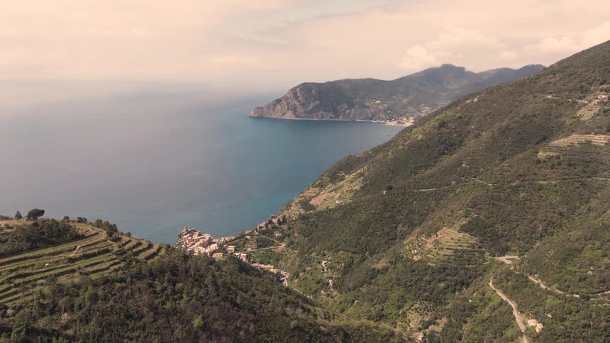 An aerial drone slowly flies over the terraced mountainsides to reveal the stunning coastal villages of Cinque Terre, Italy
