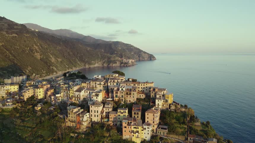 A stunning aerial view captures the picturesque village of Corniglia in Cinque Terre, Italy, perched on a cliff overlooking the calm sea at dawn