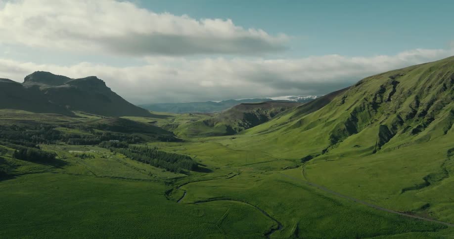 A static wide aerial view of a vast, lush green valley nestled between mountains under a partly cloudy sky