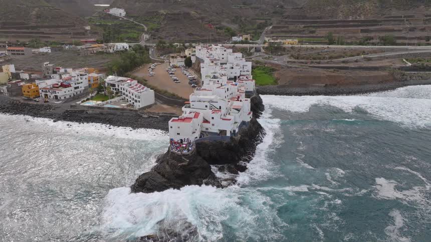 Aerial view of a picturesque white coastal village built on a rocky outcrop as waves crash against the shore