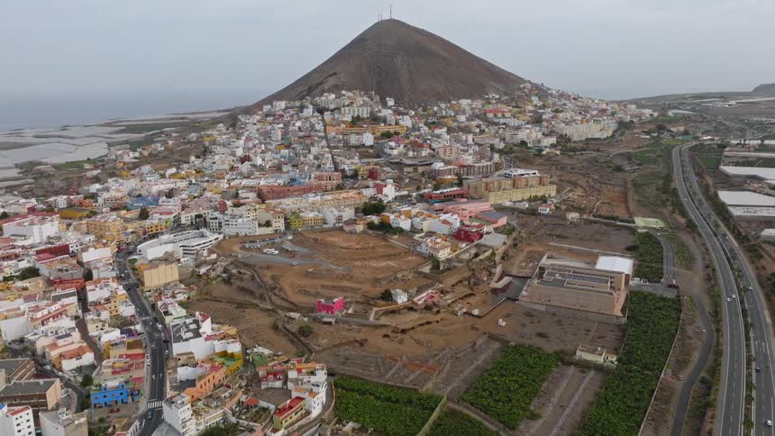 Sweeping aerial footage captures a coastal town sprawling up the side of a volcanic mountain with a major highway nearby