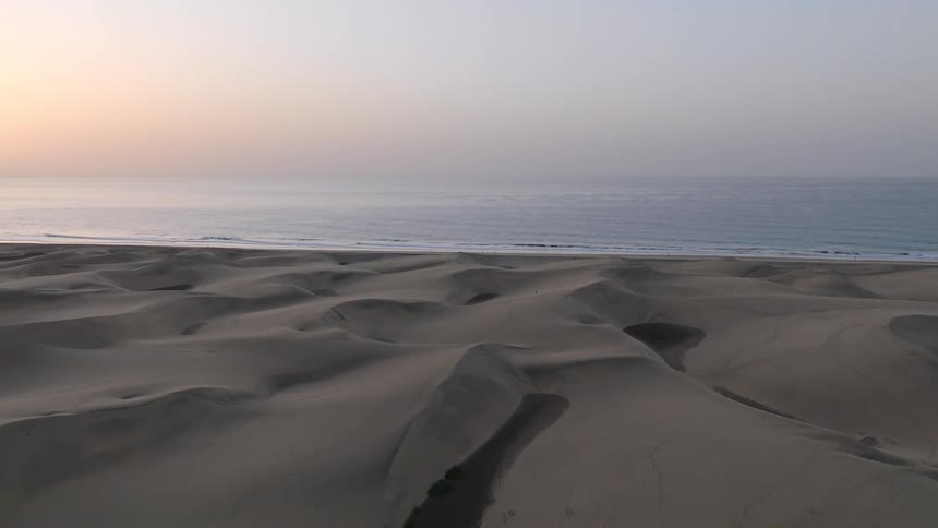 A stunning time-lapse captures the sun rising over the calm ocean next to a vast expanse of coastal sand dunes