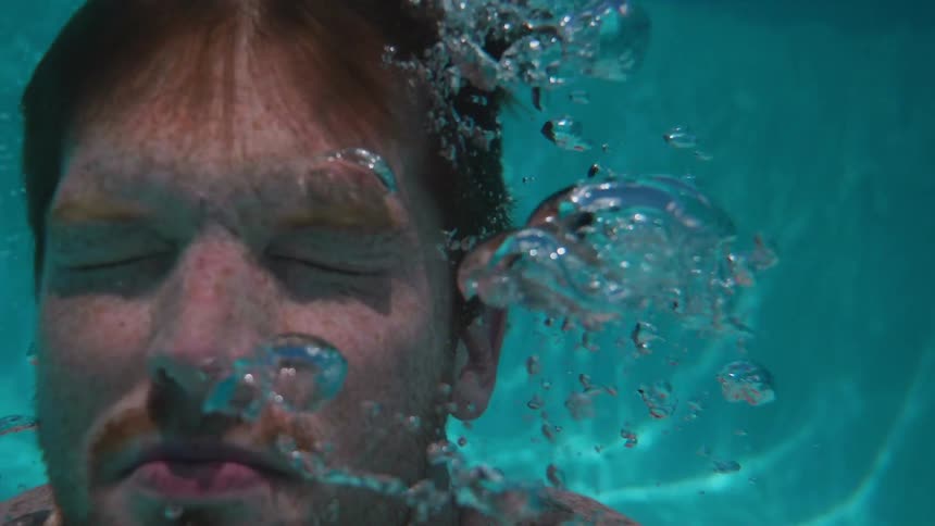 A man floats in the water blowing bubbles
