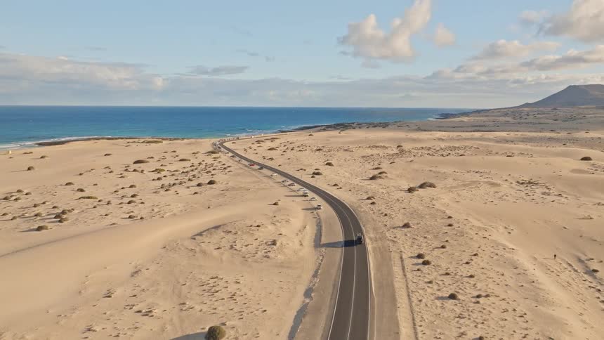 Aerial view of a scenic coastal highway winding through a vast desert of sand dunes next to the blue ocean