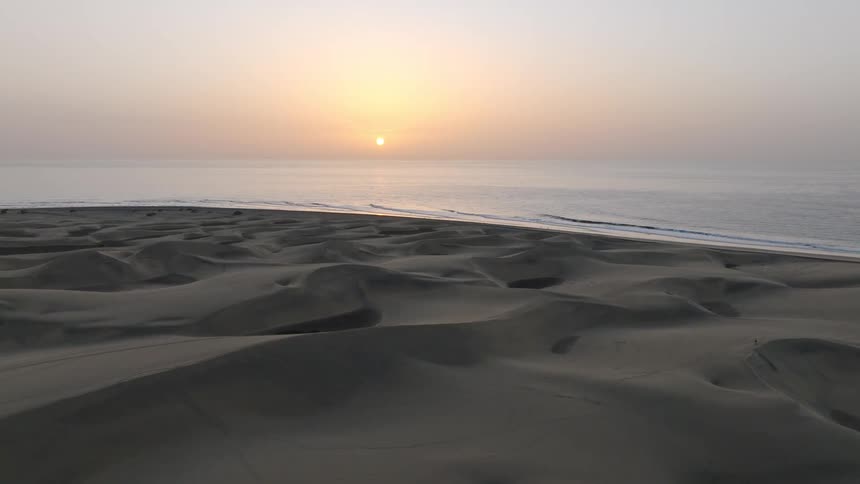 A serene wide shot of the vast Maspalomas sand dunes meeting the ocean as the sun rises on the horizon