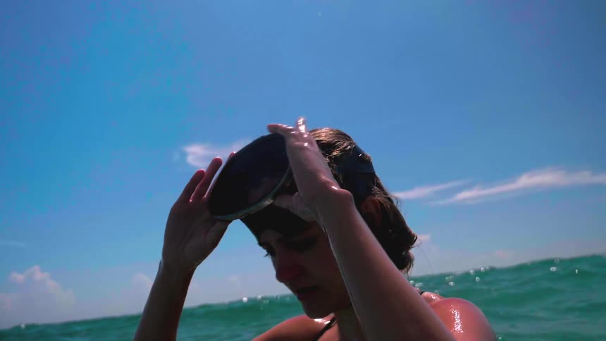 Women standing in ocean pulls her goggles down onto her face