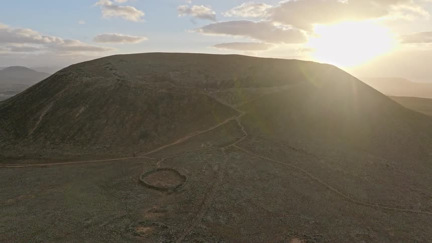 A majestic aerial view ascends to reveal the vast Calderon Hondo volcano crater in Fuerteventura as the sun rises