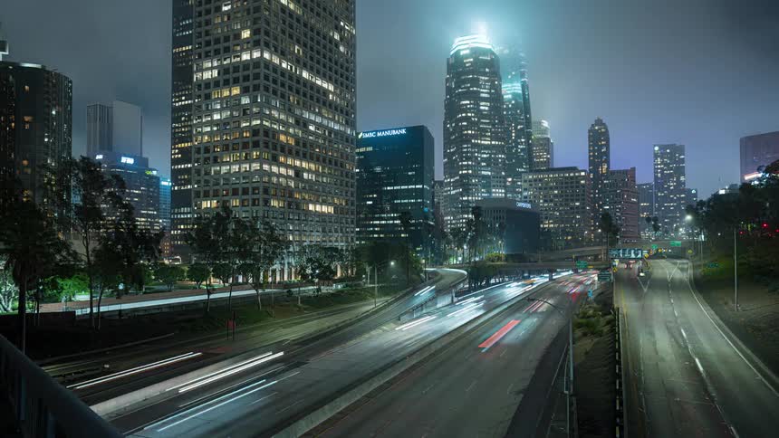 A dramatic time-lapse of traffic flowing through the 110 freeway in downtown Los Angeles at night as the camera tilts up to reveal the foggy, illuminated skyline