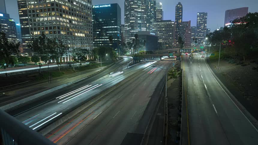 A cinematic timelapse of the downtown Los Angeles skyline and busy freeway traffic creating light trails on a foggy night