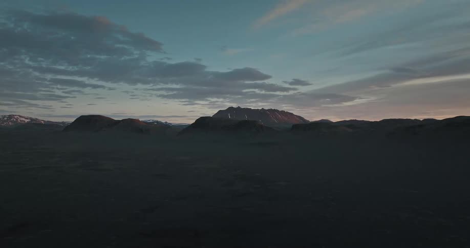 A tranquil and wide shot of a dark volcanic landscape with a distant mountain range under a twilight sky
