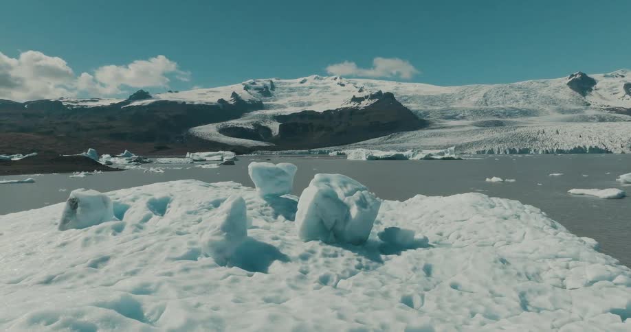 An expansive panoramic view of a beautiful glacial lagoon where icebergs float serenely in the water with snowy mountains in the distance