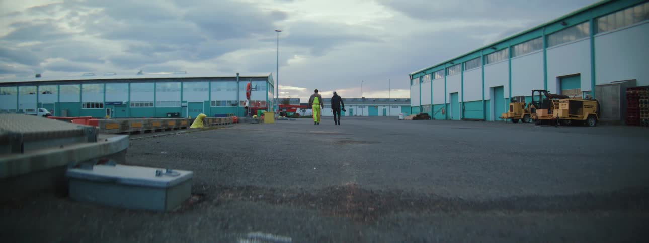 Rear view of two workers walking away through an industrial complex under a cloudy sky