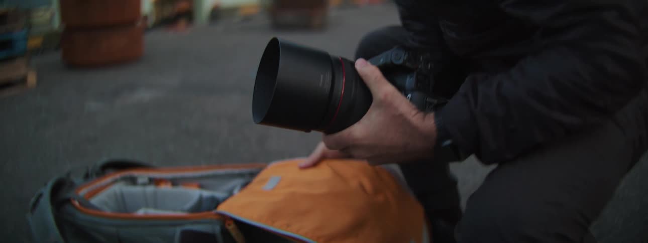 A professional photographer carefully removes his camera with a telephoto lens from its case while kneeling on a dock at twilight