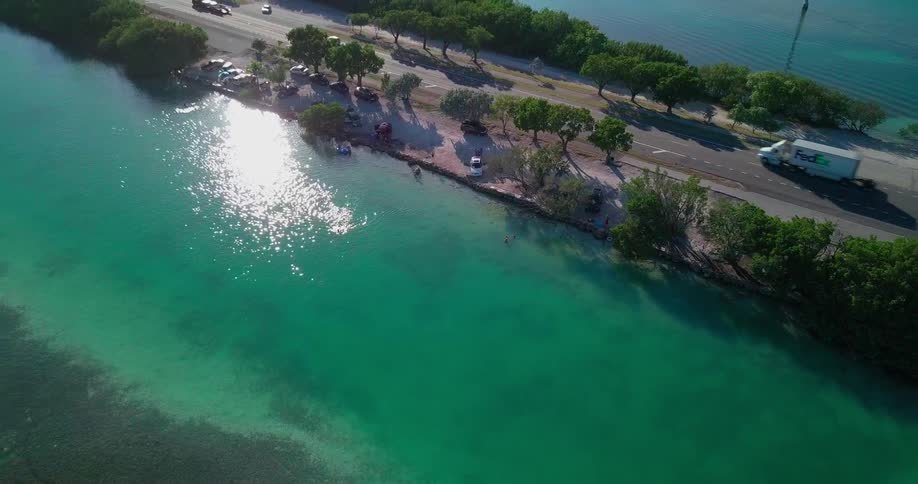 Cars driving on road surrounded by clear green body of water