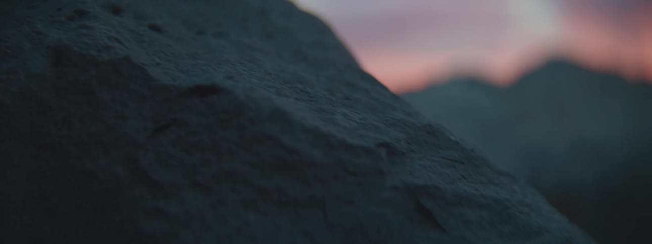 A moody and atmospheric close-up shot pans slowly over the detailed texture of a large rock during a colorful sunset