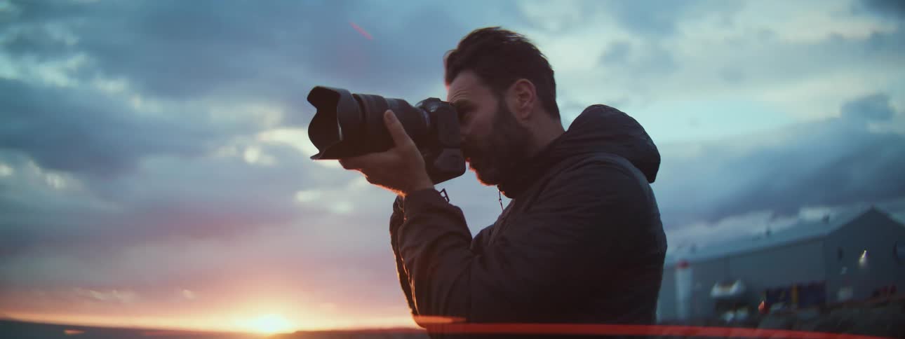 A male photographer with a professional camera frames a shot of the golden hour sunset over the ocean coast