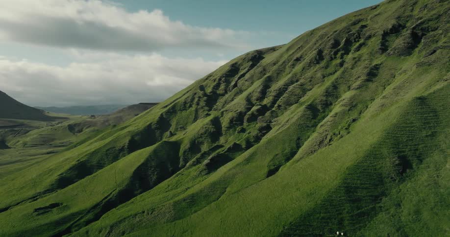 A majestic, rolling green hillside with unique textured slopes stands tall against a cloudy blue sky