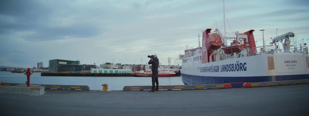 A travel photographer documents the city skyline and a large ferry from a pier in an Icelandic harbor
