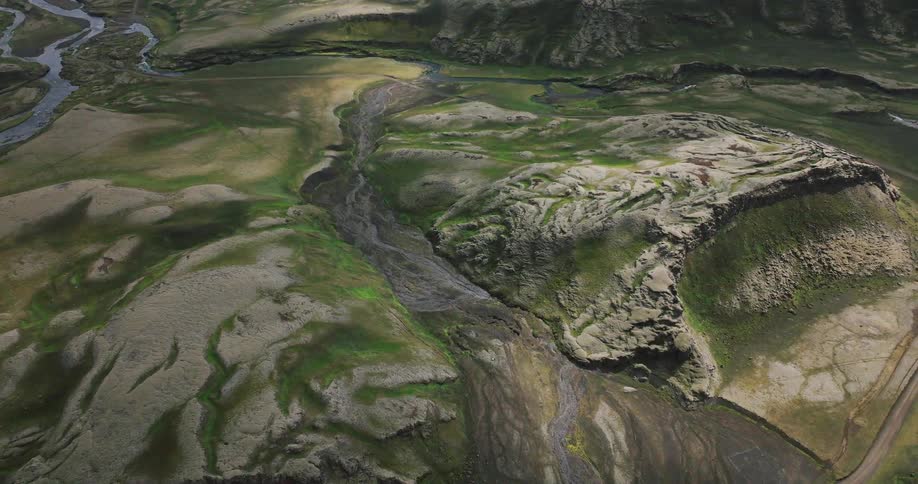 High aerial view of a vast, green Icelandic valley with a river snaking through it as cloud shadows slowly glide over the rugged terrain