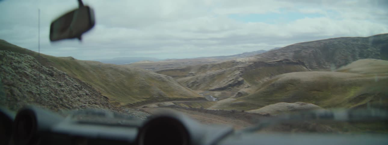 Point-of-view of an off-road vehicle navigating a bumpy dirt track through a vast, remote mountain valley